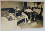 Foto Original Fotoptica (1962) Cena Familiar com Brinquedo Caminhão de Madeira AntigoEspetacular e espontâneo registro em preto e branco que captura o cotidiano de um lar no início dos anos 1960. A cena mostra um senhor idoso descansando em uma poltrona, uma mulher jovem deitada de bruços no sofá interagindo com uma criança pequena, e caixas espalhadas pelo tapete.