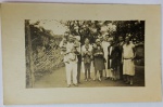 Foto Época (c. 1920/1930) Retrato de Grande Grupo Familiar  Moda dos Anos 20 com Chapéus Cloché Belíssimo e numeroso registro social capturando um grupo composto por dez pessoas (adultos, jovens e crianças de colo) posando ao ar livre, possivelmente no quintal ou jardim de uma residência de época. Riqueza de Detalhes de Época: O grande atrativo deste lote para colecionadores é a fiel representação da moda e indumentária do final da década de 1920: Moda Feminina: Destacam-se os vestidos de corte reto com cintura baixa, característicos das "melindrosas", e o uso proeminente dos icônicos chapéus estilo cloché (ajustados à cabeça) por duas das mulheres. Moda Masculina e Infantil: Inclui um homem à esquerda em trajes claros segurando duas crianças pequenas, um jovem ao centro de paletó curto e calça curta (típico da infância da época) e homens ao fundo com trajes formais.