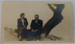 Foto Época (c. 1940/1950) Casal Elegante Sentado à Beira-Mar junto a Árvore Inclinada  Borda Canoa Elegante e sóbrio retrato que captura um casal de senhores de meia-idade posando assentados à beira-mar ou às margens de um grande lago/rio.