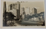 Foto Postal Histórica (c. 1950) Avenida 9 de Julho  Edifícios em Construção com Dedicatória Espetacular e raro registro urbanístico tirado a partir da Avenida 9 de Julho. A imagem captura um icônico automóvel clássico dos anos 40 em movimento e, ao fundo, grandes arranha-céus do centro da capital paulista  incluindo imponentes edifícios de apartamentos ainda com as estruturas e andaimes de construção expostos no topo, documentando o "boom" imobiliário da época. Legenda e Selo de Estúdio: Na base inferior consta: "12  SÃO PAULO  AVENIDA 9 DE JULHO" e a assinatura do estúdio no canto direito: "FOTO POSTAL COLOMBO"