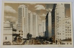 Foto Postal Histórica (c. 1950) Rua São Luiz  Edifício Roosevelt com Riquíssima Dedicatória Impressionante e raro registro urbanístico que captura a monumental perspectiva da Rua São Luiz. À esquerda, destaca-se a arquitetura clássica do palacete do antigo Instituto de Educação Caetano de Campos. Ao centro e à direita, erguem-se os novos e imponentes arranha-céus residenciais e comerciais com automóveis clássicos dos anos 40 estacionados ao longo da via. Legenda e Selo de Estúdio: Traz impresso na base esquerda: "RUA SÃO LUIZ  SÃO PAULO" e a assinatura da renomada editora no canto inferior direito: "FOTOLABOR".