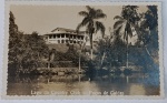 Foto Postal do Country Club Poços de Caldas Datada (1954) com Rica Mensagem "Amiga da Onça" Registro paisagístico clássico mostrando o espelho d'água e a sede colonial do Country Club de Poços de Caldas. Riquíssimos Detalhes do Verso (Transcrição Íntegra):O verso destaca-se pelo uso descontraído e carinhoso de uma famosa gíria da época, inspirada na célebre personagem dos quadrinhos de Péricles Maranhão (O Amigo da Onça, muito popular na revista O Cruzeiro nos anos 40 e 50):