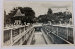 Foto Postal Época (c. 1930/1940) Entrada e Canal do Parque das Águas de Caxambu - MG Belíssimo e clássico registro monumental que documenta a icônica entrada principal do Parque das Águas de Caxambu - MG. A composição destaca em perspectiva o canal central canalizado em concreto com balustradas decorativas geométricas. Ao fundo, avista-se o pórtico com os dizeres "Parque das Águas", um suntuoso pavilhão de linhas ecléticas à esquerda, pedestres de época passeando e a torre de captação/relógio à direita.