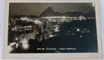 Foto Postal Noturna Época (c. 1950) Vista Panorâmica de Botafogo e Pão de Açúcar Iluminados Belíssimo e imponente registro noturno que captura o "boom" de verticalização e o traçado luminoso da Zona Sul do Rio de Janeiro - RJ. A tomada em ângulo elevado destaca em primeiro plano o mar de edifícios residenciais iluminados do bairro de Botafogo.