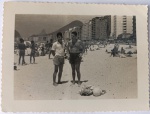 Foto Época (c. 1950) Rapazes na Praia de Copacabana com Edifícios e Bola de Gomos  Borda Canoa: Espetacular e nostálgico registro do cotidiano na Praia de Copacabana, no Rio de Janeiro - RJ. A cena captura em primeiro plano dois rapazes em trajes de banho da época (um de calção claro e camisa social de mangas curtas e o outro de calção escuro), posando na areia ao lado de seus pertences e de uma clássica bola de futebol de gomos brancos antiga.