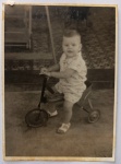 Foto Época (c. 1950/1960) Criança em Triciclo Velocípede Antigo de Metal  Brinquedo VintageEncantador e nostálgico registro do cotidiano infantil de meados do século XX. A cena captura um menino pequeno posando montado em um clássico triciclo / velocípede infantil antigo de metal tubular.