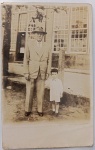 Fotografia Vintage  Avô/Pai e Criança em Frente a Casarão de Época (c. 1940-1950)Bela fotografia original de época, em formato vertical e plano inteiro, capturada em ambiente externo. A imagem registra um senhor elegante vestindo terno social claro completo (paletó e calça de alfaiataria), camisa, gravata estampada e chapéu de feltro clássico estilo Fedora. Ele está de mãos dadas com um menino pequeno, vestido com conjunto infantil claro de bermuda e camisa, adornado com uma gravata borboleta e boina escura.