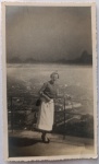 Fotografia Vintage (1951)  Turista no Morro da Urca / Pão de Açúcar (Rio de Janeiro)Espetacular fotografia original de época, capturada em formato vertical com as clássicas bordas recortadas em estilo guilhotina (ziguezague). A imagem registra uma elegante senhora posando no mirante do Morro da Urca, no Rio de Janeiro. Ela veste trajes típicos da moda feminina do início dos anos 1950, compostos por saia midi clara estruturada, blusa de mangas curtas, sapatos de salto escuros e traz uma bolsa de lado a tiracolo.