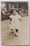 Fotografia Vintage (1954)  Menina "Celia Regina" com Gansos (Rio de Janeiro) e DedicatóriaEncantadora e dinâmica fotografia vernacular original de época, em formato cartão-postal vertical com bordas recortadas em estilo guilhotina (ziguezague). A imagem registra em ambiente externo a pequena Celia Regina caminhando e sorrindo em direção à câmera. Ela veste um lindo vestidinho claro de mangas bufantes, meias brancas e sapatinhos de fivela escuros.