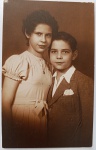   Retrato de Família / Irmãos Identificados. Retrato de estúdio dos irmãos Odette Oliveira Develly e Ary de Oliveira Develly (o mesmo menino "Wessel" registrado em foto anterior de 1936). Odette veste um elegante vestido claro com mangas bufantes, colar com pingente e laço na cintura. Ary veste paletó de tweed com lenço de bolso estruturado e camisa de colarinho aberto.