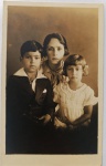  Retrato de Família / Irmãos e Primos Identificados. Retrato de estúdio de três crianças/jovens, destacando o menino Wessel (Ary de Oliveira Develly) na infância à esquerda, uma jovem ao centro (Mariinha) usando um grande laço de fita no pescoço, e uma menina menor à direita vestindo um trabalhado vestido claro de pregas e renda. Inscrições no Verso: Belíssima dedicatória poética manuscrita a tinta, utilizando a grafia da época ("affectuosa"), direcionada a Alcidia e Homero, assinada por Mariinha. Datada de "Maceió, 16/9/34". Presença da marca d'água/divisória "WESSEL".