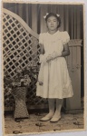   Imigração Japonesa / Formatura Escolar ("deploma"). Retrato de estúdio da jovem nipo-brasileira Cijiuco aos 11 anos de idade. Traje de gala infantil completo com vestido claro de pregas e luvas brancas, segurando o diploma em formato de canudo. Cenário rico com treliça de madeira, coluna e vaso de vime. Inscrições no Verso: Rica dedicatória manuscrita a lápis/tinta destinada à sua professora, Dona Helena, registrando a data e o motivo. Presença do carimbo comercial do Foto Astor e da tradicional divisória impressa "WESSEL".