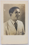   Retrato Masculino / Moda Masculina de Época / Retrato Identificado. Retrato de estúdio em plano médio de perfil de um jovem adulto sorridente, identificado fisionomicamente como Wessel (Ary de Oliveira Develly) na maturidade. Ele veste um elegante traje de alfaiataria composto por paletó claro de lapela larga, camisa de colarinho pontudo e gravata escura com padronagem geométrica repetida. Cabelo curto penteado para trás com fixador de época. Características Físicas: Fotografia original em preto e branco (gelatina de prata), montada no formato clássico de cartão-postal com a marca de papel "WESSEL" na divisória do verso. Textura de emulsão ligeiramente reticulada/fosca. Corte reto tradicional.