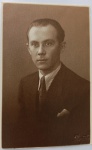   Retrato Masculino / Moda dos Anos 30 / Identificado. Retrato de estúdio em plano médio de busto do jovem Angelo. Ele posa com expressão séria e elegante, vestindo paletó escuro de alfaiataria, camisa de colarinho estruturado com fina padronagem listrada, gravata escura lisa e lenço claro estruturado no bolso da lapela. Cabelo curto com corte clássico penteado para trás. Inscrições no Verso: Dedicatória manuscrita à tinta azul, assinada pelo retratado ("Angelo"), direcionada a Dona Maria Augusta, José e familiares, datada de "18-9-937". Divisória central com a marca de papel postal "Agfa". No canto superior esquerdo do verso, há um pequeno carimbo numérico ou de inventário antigo esmaecido.