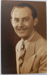  Retrato Masculino / Moda dos Anos 30 / Identificado. Retrato de estúdio em plano médio de busto do jovem Angelo, aqui posando sorridente e ostentando um bigode fino característico da época. Veste paletó claro com textura em xadrez miúdo, camisa clara e uma vistosa gravata estampada com padrão geométrico em diagonal. Cabelo curto penteado para trás com fixador. Inscrições no Verso: Rica dedicatória manuscrita à tinta preta, assinada pelo retratado ("Angelo"), direcionada à sua amiga Dona Maria Augusta e filhos. Datada de "9-4-938". Canto inferior direito com a marca d'água em relevo da fabricante belga "Gevaert Ridax".