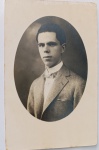   Retrato Masculino / Moda Masculina Antiga / Linha Familiar Anterior. Retrato de estúdio em plano médio de três quartos de um jovem senhor, identificado fisionomicamente como parte da linhagem ascendente da família Develly/Wessel. O retratado exibe trajes de alta alfaiataria do início do século XX, destacando o paletó de tweed claro, colarinho alto duro e gravata borboleta miniatura listrada. Características Físicas: Fotografia original em preto e branco com suave pátina do tempo. Apresenta uma máscara fotográfica de revelação em formato oval perfeito, emoldurada pelas margens brancas originais do papel-cartão. Corte reto tradicional.