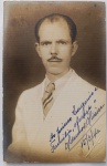  Retrato Masculino / Moda dos Anos 40 / Identificação Familiar / Sobrenome Oliveira. Retrato de estúdio em plano médio de busto do senhor Aldenor Oliveira, posando de frente com expressão séria. Ele veste paletó claro de alfaiataria de verão, gravata listrada e ostenta bigode fino típico da época. Inscrições na Frente: Rica dedicatória manuscrita à tinta azul na base direita da imagem: "Ao primo Eugenio e Familia, oferece o Aldenor Oliveira. 15/3/40.", consolidando a árvore genealógica e o sobrenome Oliveira no acervo.
