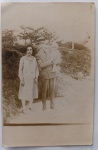   Retrato de Família / Maternidade e Paternidade / Moda dos Anos 20 / Chapéu Boater / Identificação Familiar. Retrato vernacular em plano inteiro de um jovem casal com seu bebê em um ambiente de campo ou encosta arborizada ao ar livre, destacando o pai com chapéu canotier e a mãe com vestido plissado de época. Características Físicas: Fotografia original em tom sépia médio com revelação em máscara retangular estruturada por margens brancas originais. Corte reto tradicional.