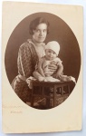  Moda Masculina dos Anos 40 / Vida Urbana / Retrato Identificado / Família Oliveira Develly. Registro instantâneo de calçada mostrando o jovem Wessel (Ary de Oliveira Develly) de terno branco ao lado do patriarca sênior da família de terno escuro e chapéu fedora, caminhando sobre calçada de pedras portuguesas. Características Físicas: Fotografia original em preto e branco com tom sépia suave, formato de cartão-postal vertical com corte reto tradicional. Apresenta pequenos furos circulares de fixação antigos na polpa do papel (um no topo superior central e outro na altura do terno branco).