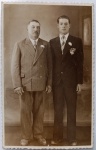  Retrato de Família / Paternidade / Imigração e Genealogia / Família Estevão. Retrato formal de estúdio de pai e filho na Patagônia, destacando o pai à esquerda de terno claro transpassado e o filho à direita de terno escuro com lenço xadrez, ambos com flores (boutonnière) na lapela. Inscrições no Verso: Inscrição manuscrita à tinta identificando o destinatário no Brasil: "Exmo. Snr. Vital Estevão", acompanhada da datação precisa. Traz as linhas guias de preenchimento de cartão-postal ("Tarjeta Postal" esmaecido) e bordas recortadas em padrão serrilhado (deckle edge) nos quatro lados.