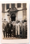  Fotografia Antiga / Cartão-Postal Fotográfico Vernacular (Real Photo Postcard - RPPC). Época Estimada: Circa 19451955 (Pós-Guerra / Metade do século XX). Procedência Geográfica: Rio de Janeiro - DF (Época da Capital Federal). Marco Arquitetônico: Fachada e portal colonial da Igreja de Nossa Senhora do Rosário dos Pretos. Tema: Retrato Masculino Coletivo / Solenidade Religiosa / Moda dos Anos 40 e 50 / Identificação Familiar. Retrato em plano inteiro de cinco cavalheiros elegantes posando no adro da histórica igreja carioca ao lado de um automóvel de época, exibindo sobretudos, suéteres e ternos de alta alfaiataria.