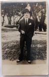   Fotografia Antiga / Fotografia de Rua Vintage (Street Snapshot / Lambe-Lambe). Época Estimada: Circa 19371945. Procedência: Provável Rio de Janeiro ou Santos (Eixo principal do círculo de Angelo). Tema: Retrato Masculino / Moda dos Anos 30 e 40 / Chapéu Fedora / Retrato Identificado / Círculo de Maria Augusta. Retrato vernacular em plano inteiro do jovem Angelo posando com um cigarro na mão em um parque público arborizado, exibindo terno de alta alfaiataria e chapéu de feltro.