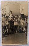  Fotografia Antiga / Cartão-Postal Fotográfico de Bordo (Real Photo Postcard - RPPC). Data Exata: 1946 (Pós-Guerra). Procedência: Registro de bordo em alto-mar (Navio Transatlântico). Conexão direta com o lote anterior em papel italiano Ferrania. Tema: Vida Marítima / Cruzeiros de Época / Batismo de Netuno / Cruzamento do Equador / Curiosidades Históricas. Registro fotográfico vernacular espontâneo mostrando o cortejo da trupe de Netuno com megafone e prato de percussão celebrando o batismo da passageira coroada no convés do navio.