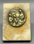 ARTE SACRA - Objeto decorativo ou oratório de mesa. (Nota: O material da base é comumente classificado comercialmente como alabastro, ônix ou mármore natural). Placa retangular em pedra natural em tons amarelados, aplicada com medalhão circular em metal relevado e patinado, com assinatura (atribuída ao renomado escultor e medalhista francês Émile Dropsy), representando cena religiosa de Primeira Comunhão com a figura do Espírito Santo em forma de pomba e figuras ajoelhadas em oração. O verso possui chapa metálica de proteção e suporte articulado duplo. A peça apresenta acentuada oxidação e ferrugem no suporte traseiro, além de desgastes naturais pelo tempo. Med. 8x6 cm.