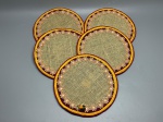 DIVERSOS - Jogo com 5 sousplats (ou jogos americanos redondos) confeccionados artesanalmente em base de juta natural em tom cru. Cada peça possui borda circular decorada com faixa em tecido bordado e aviamentos em tons de vinho e amarelo, guarnição de passamanaria em renda floral dourada/bege formando um círculo interno, e acabamento central com uma pequena aplicação de flor em rococó de fita com folhas verdes. Dia. 24 cm.