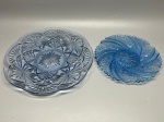 DEMI CRISTAL - Dupla de travessas ou pratos decorativos redondos em vidro prensado na cor azul translúcido (azul claro/pastel), com ricos relevos geométricos e florais em estilo lapidado vintage. Inclui um prato maior com padrão de estrelas e leques interligados e borda ondulada, e um prato menor com padrão radial em espiral (tipo swirl) com medalhões centrais estriados. Peças em excelente estado de conservação. Dia. 28 cm e 21 cm.