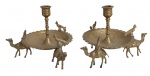 Par de castiçais orientais em bronze dourado, de formato circular, decorados com figuras de camelos e motivos em relevo. Peças de caráter exótico e ornamental. Medidas: 16 x 12 cm.