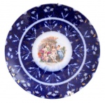COMPANHIA DAS INDIAS - Magnifico medalhão em porcelana policromada adornada com ramalhetes de flores sobre azul cobalto com detalhes em vibrante ouro com desgaste e cena de ninfas ao centro. Meados século XIX. Possui perda na garra do suporte. Mede 30, 5 cm.