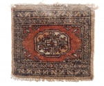 TAPETE ORIENTAL ANTIGO, em lã, com decoração geométrica, campo central em tom vermelho terroso e bordas ornamentadas, apresentando sinais de uso e desgaste compatíveis com a idade. Virada do século. Mede 30 x 33 cm.