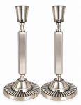 BRISTOL, par de castiçais em metal espessurado a prata, de origem inglesa, estilo clássico, com fustes retangulares, copos de perfil cônico com decoração canelada e bases circulares ricamente trabalhadas com motivos radiais. Peças de elegante desenho e acabamento, características da produção inglesa. Mede 23 cm