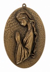 Medalhão oval em bronze, em alto-relevo, com figura feminina provavelmente santa, em oração, pátina de época e textura radial. Possui argola para suspensão. Mede 16,5 x 11 cm.