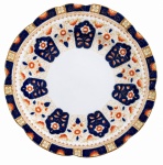CROWN  - Prato raso de formato circular com borda recortada, em porcelana inglesa, decorado ao estilo Imari, em rica composição de azul-cobalto, laranja, branco e dourado. Apresenta reservas florais, arabescos e elementos ornamentais distribuídos de forma simétrica, com delicada pintura à mão e filetes dourados. No verso, marca CROWN, sob coroa, com monograma W.L.L. Meados século XIX. Medida: 20 cm de diâmetro.