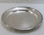 WOLFF- Grande bandeja redonda em metal espessurado a prata, fundo liso, borda decorada padrão laço de fita cruzada. Med. 3,5 x 39 cm diâmetro.