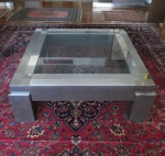 Mesa para frente de sofá em madeira revestida em placas de aço escovado , ao centro vidro embutido no formato quadrangular. Faltando quatro acabamentos de aço nos pés. Med 41 x114 x 114. RETIRADA POR CONTA DO ARREMATANTE NA PRAIA DO FLAMENGO COM AGENDAMENTO