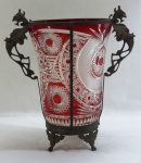 BOHÊMIA - Vaso em cristal double rubi lapidado a mão, com padrões geométricos, florais com rosetas, palmas e sulcos bisotados, guarnecido em estrutura de bronze, suporte e alças no formato de dragões alado, quatro pés em garra. Med. 32 x 30 cm.