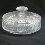 Bombonier em cristal translúcido da Bohêmia ricamente lapidado a mão com rosetas e sulcos, tampa com pega diamante. Com infímo quase imperceptível bicado na borda interna. Med. 23 x 20 cm.