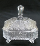 Bombonier em demi cristal no formato retangular octagonal, decorado com rosetas, palmas e ranhuras, quatro pés caracol, tampa com pega alongada estilo diamante. Med. 15 x 14 x 12 cm.