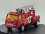 Miniatura die-cast de uma carrinha de bombeiros (Fire Engine, modelo SS 501-4, escala 1/58), fabricada na China. Apresenta carroçaria em tom vermelho com vidros âmbar/amarelados, escada telescópica principal cromada montada na parte superior traseira, mangueira branca enrolada na lateral, detalhes de equipamento de combate a incêndios gravados na carroçaria e chassi inferior em plástico preto com inscrições de fabrico e escala. Com marcas de tempo de uso.