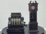 Conjunto de duas miniaturas decorativas afia-lápis em metal/die-cast com acabamento em tom de bronze envelhecido, fabricadas em Hong Kong ("MADE IN HONG KONG"). O conjunto é composto por uma réplica em miniatura de caixa registadora antiga do modelo National, com gravuras em relevo, manivela lateral, rolos de valores e topo marcado com "CASH SALES", e uma miniatura de relógio de pêndulo clássico com mostrador de numeração romana e ornamentos esculpidos na estrutura. Ambos os itens funcionam como afia-lápis colecionáveis, possuindo lâmina e orifício na base/traseira. Com marcas de tempo de uso.