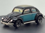 Miniatura die-cast do Volkswagen VW Beetle de 1962 (Matchbox, Mattel, escala 1/58), com pintura bicolor em preto e azul-petróleo e teto de abrir cinzento. Apresenta pormenores como para-choques e estribos cromados, inscrição "MATCHBOX" no para-brisa frontal, jantes desportivas de cinco raios e chassi inferior em metal gravado com as especificações do fabricante e escala. Com marcas de tempo de uso.