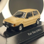 Miniatura colecionável em die-cast (metal com pormenores em plástico) referente ao emblemático hatchback Fiat Uno do ano de 1983. Apresenta acabamento em pintura na cor bege. Destaca-se pelo fiel detalhamento da carroçaria de duas portas, incluindo a grelha frontal com as cinco barras diagonais características da marca, faróis dianteiros e piscas em acrílico translúcido, para-choques pretos, retrovisor em destaque, limpador de para-brisas em miniatura e placa identificativa "Fiat Uno". Equipado com jantes prateadas replicando o modelo original e pneus em borracha. Encontra-se fixado sobre base expositora rígida na cor preta, com a identificação do modelo gravada em letras prateadas na parte frontal.   Item em excelente estado geral de conservação, com estrutura e pintura íntegras, sem faltas nem descasques. Vidros acrílicos preservados e base expositora em perfeito estado com a serigrafia limpa.   Medidas: 3 cm (altura)  8 cm (comprimento)  3 cm (largura).