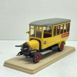 Miniatura die-cast do clássico autocarro histórico Magirus Bus de 1919 da marca Eligor (ref. 3002). Apresenta pintura em amarelo vivo com teto cinzento, inscrições laterais "Meiringen Grimsel Brig", detalhes em madeira nas janelas, matrículas suizas "P-20", base expositora com caixa acrílica de proteção e etiqueta autocolante original da loja "Aux Modélistes" em Angers. Com marcas de tempo de uso.