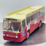 Miniatura colecionável em die-cast (metal com pormenores em plástico) na escala 1/43, referente ao clássico autocarro urbano Leyland Verheul. Apresenta pintura bicolor em encarnado na parte inferior e bege/creme no teto e zona superior das janelas. Destaca-se pelo elevado nível de detalhe e caracterização de época, incluindo letreiro frontal com a rota "6 vinkhuizen-noord", painéis publicitários no teto ("L. de Vries Jr. - TOGA JACQUET SMOKING ROK") e nas laterais ("werkplan uitzendburo", entre outros), limpadores de para-brisas em miniatura, faróis circulares dianteiros, espelhos retrovisores e matrícula identificativa "BB-87-69". As jantes surgem em tom bege com miolo encarnado, equipadas com pneus em borracha sulcados.   Item em excelente estado geral de conservação, com estrutura e pintura bastante preservadas, grafismos e autocolantes publicitários íntegros. Interior visível com assentos e volante detalhados em tom avermelhado através do acrílico translúcido dos vidros. O chassis inferior rígido em plástico preto apresenta a gravação original da escala e modelo "1/43 LEYAND VERHEUL".