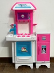 Conjunto de cozinha infantil de brinquedo da marca Magic Toys, em plástico nas cores rosa, branco e azul. Composto por módulo de cozinha com fogão simulado de quatro bocas, forno com porta translúcida, micro-ondas, pia com torneira decorativa e prateleira superior, além de módulo de geladeira de duas portas com dispensador de gelo decorativo e adesivos ilustrativos. Ambos os módulos possuem base com apoios. Apresenta marcas de uso. Não acompanha acessórios adicionais visíveis nas imagens.
