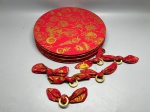 Lote composto por seis sousplats circulares e seis porta-guardanapos, em tecido vermelho com estamparia em dourado representando motivos orientais, incluindo lanternas, flores e elementos decorativos. Os sousplats apresentam estrutura rígida revestida pelo tecido estampado. Os porta-guardanapos são formados por argola de material claro, possivelmente resina ou osso sintético, envoltos pelo mesmo tecido em nó decorativo. Peças em conjunto formando aparelho de mesa temático. Estado de conservação aparentemente bom, sem danos visíveis nas imagens. base de prato, anel para guardanapo, aparelho de mesa, prato de apresentação, conjunto oriental