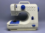 Máquina de costura portátil, marca InCasa, modelo Compact. Carcaça em plástico nas cores branco e azul, com alça superior para transporte. Painel frontal com seletor de pontos numerado de 1 a 8, botões de seleção em plástico branco, dial regulador em azul e chave de velocidade com posições L, OFF e H. Base com régua graduada em polegadas. Apresenta área de bobina com tampa azul, calcador metálico e mecanismo de tensão lateral. Observam-se marcas de uso e pequenas manchas na carcaça. Estado de conservação regular. Não acompanha acessórios visíveis nas imagens. máquina de costurar, equipamento de costura, costureirinha, mini máquina de costura